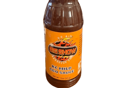Bottle of Big Show KC Mild BBQ Sauce with orange label on a textured background.
